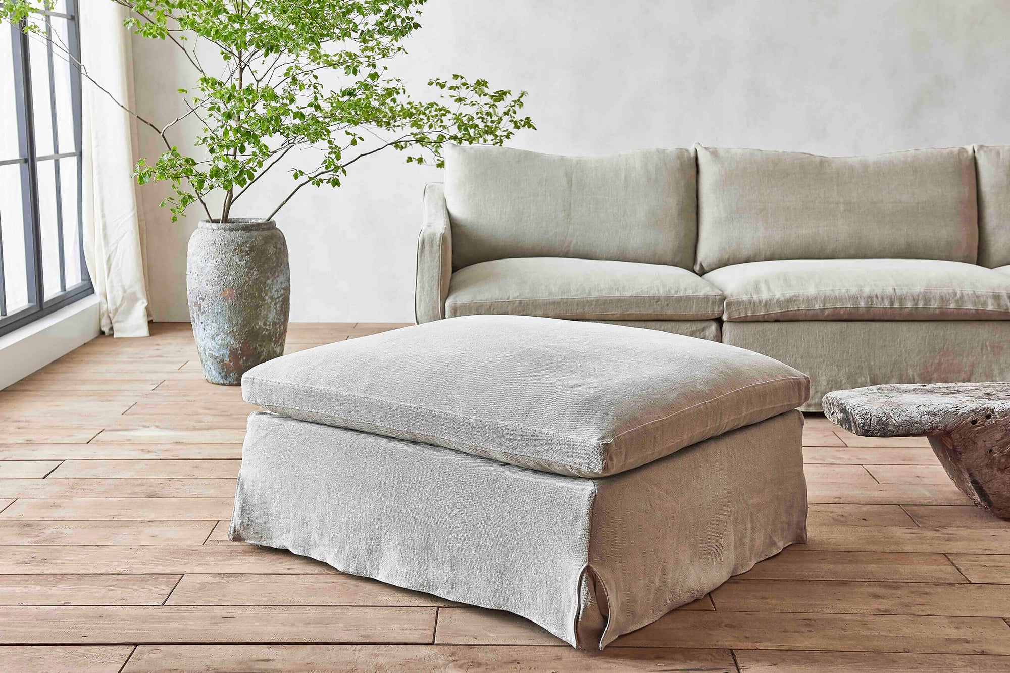 Amelia Sectional Ottoman in Jasmine Rice, a light warm greige Medium Weight Linen, placed in a room with the Amelia Sectional Sofa