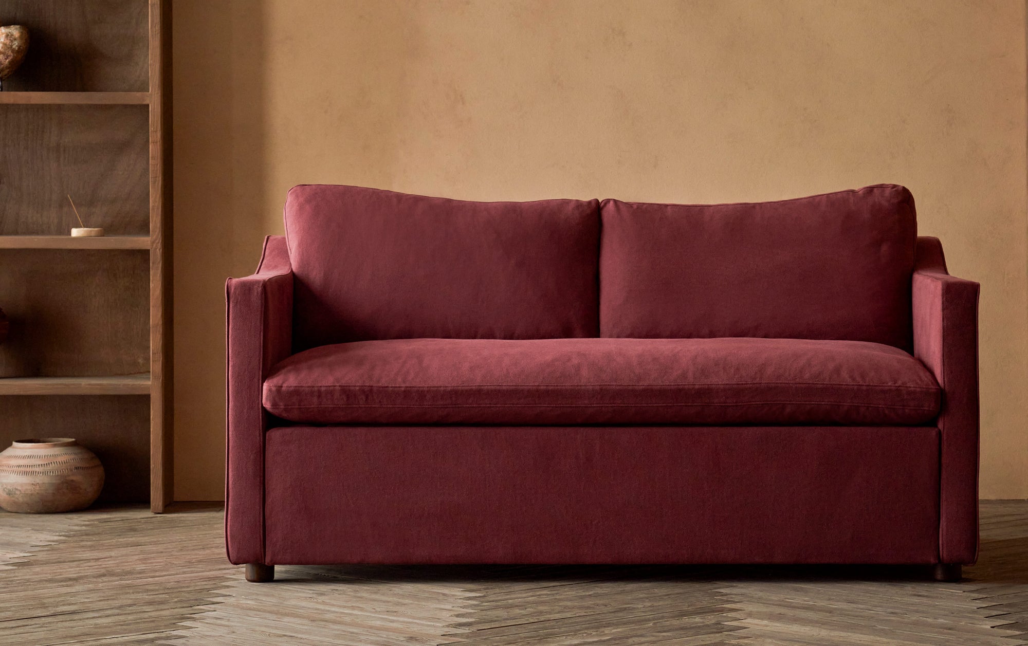 Amelia Sleeper Sofa in Summer Plum, a soft maroon Thread-Dyed Cotton Linen, with a bookcase in the background.