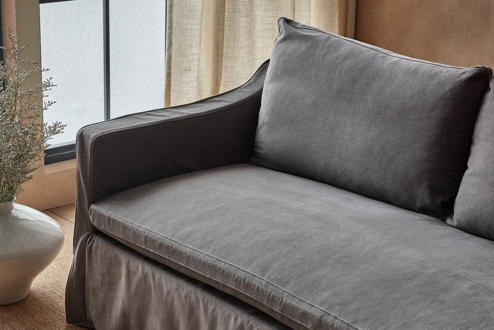 Close up of Amelia 84" Sofa Ink Cap, a medium cool grey Light Weight Linen, placed in front of a window next to a vase of flowers