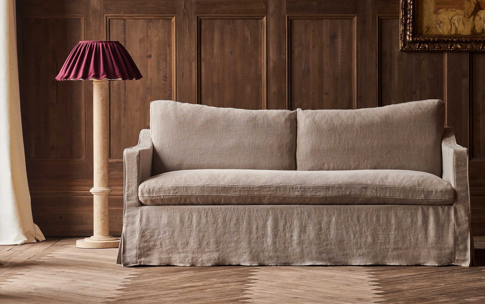 Amelia 72" Sofa in Oat Flour, a medium taupe Light Weight Linen, placed in a naturally lit, wood paneled room, next to a floor lamp