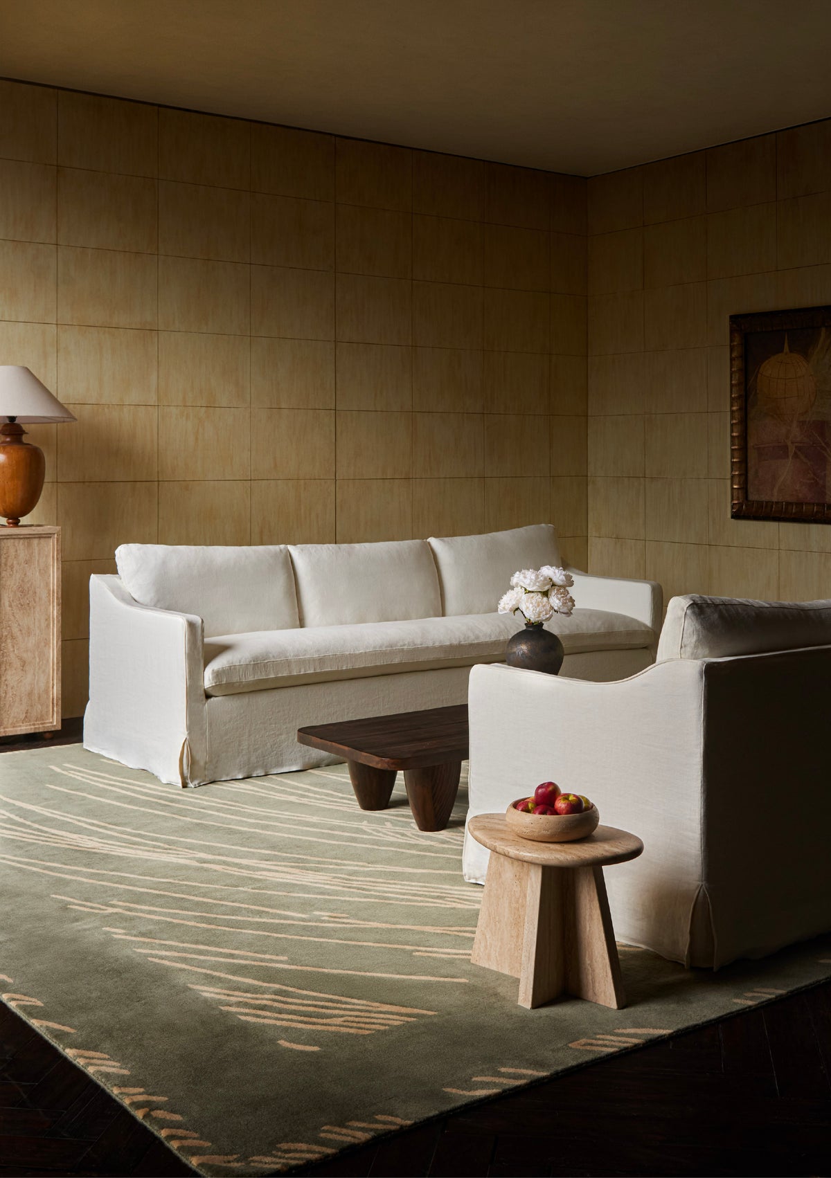 A styled living room featuring a Sixpenny Amelia sofa in water lily,  arranged on a Sixpenny  Willow hand-knotted wool mallard rug with a dark wood coffee table and a small wooden side table holding a bowl of fruit.
