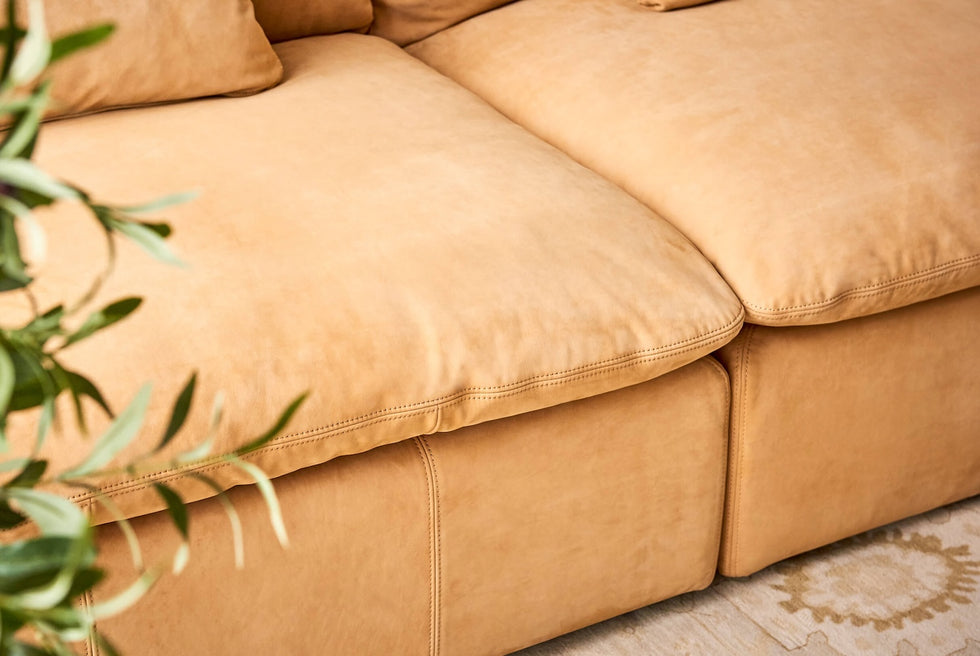 Close up of Aria Leather Sectional Sofa in Mojave Glow, a tan Meridian Leather, with a tall plant peeking into the frame
