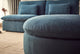 Slide #3 Close up of Aria Round Leather Ottoman in North Atlantic, a dark teal blue Meridian Leather placed on a beige rug in front of the Aria Leather Sofa in North Atlantic