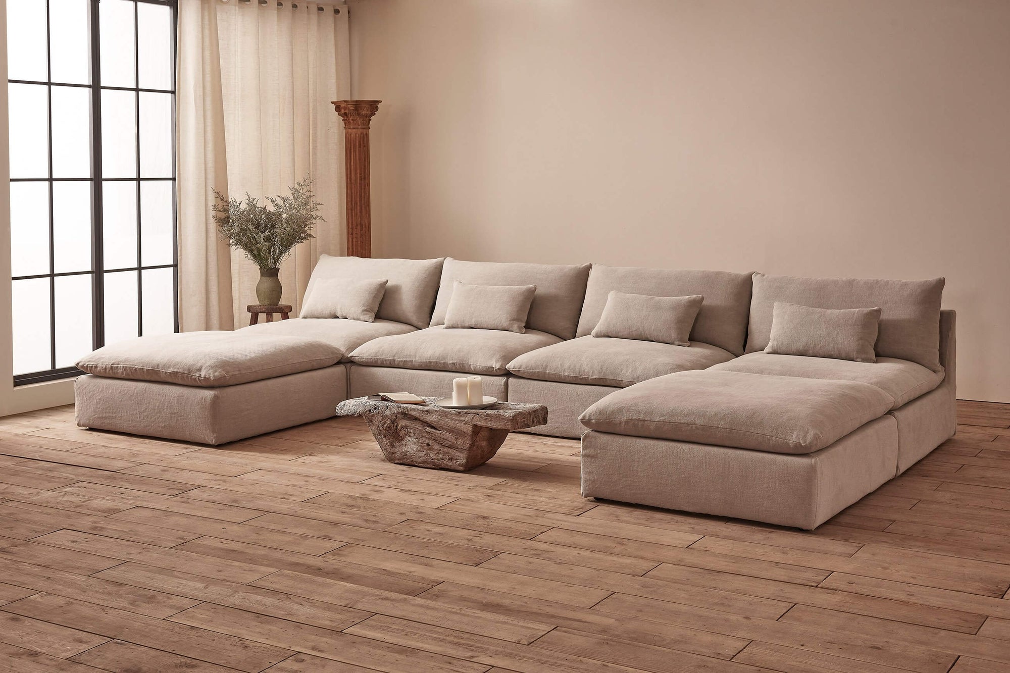 Aria U-Shape Sectional Sofa in Jasmine Rice, a light warm greige Medium Weight Linen, placed in a room with a small stone coffee table and a vase of flowers