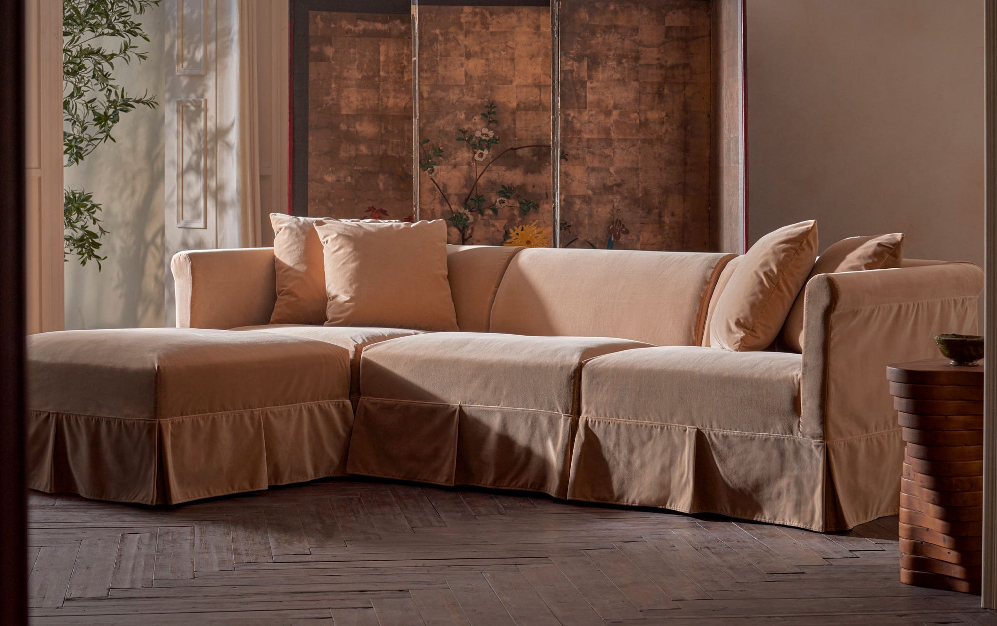 Dalia 4pc Chaise Sectional in Daily Bread, a warm, golden brown Washed Cotton Velvet, placed in a sunlit room with a painted screen and stone side table