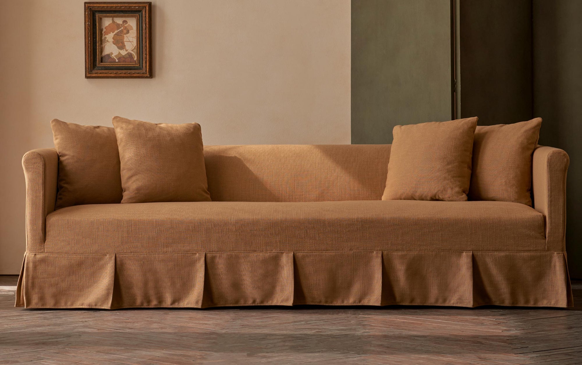 Dalia 96" Sofa in Branch Out, a golden brown linen-like recycled polyester, placed in a warmly lit room decorated with a framed picture and a folding screen