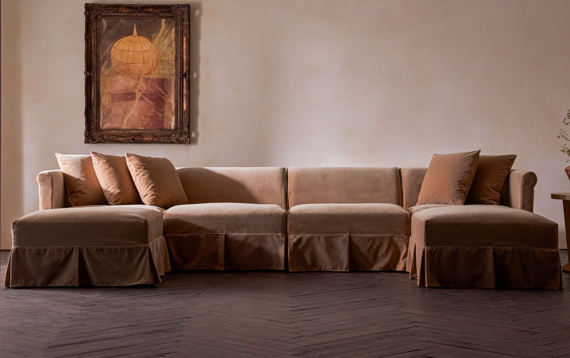 Dalia U-Shape Sectional in Daily Bread, a warm, golden brown Washed Cotton Velvet, placed in a sunny room in front of a large framed painting.