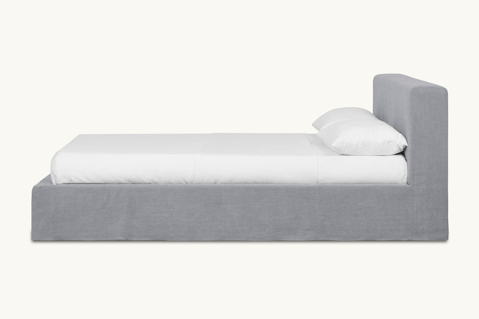 Side view of Devyn Queen Bed Frame in Ink Cap, a medium cool grey Light Weight Linen, made up with white linen bedding