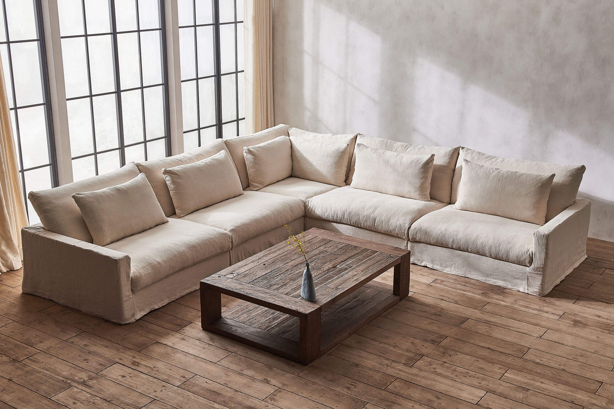 Devyn Corner Sectional Sofa in Corn Silk, a light beige Washed Cotton Linen, plaved in front of a large window with a wooden coffee table