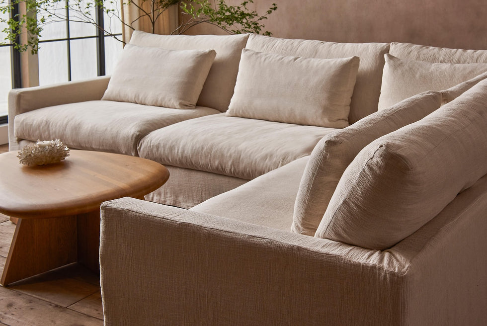 Close up of Devyn L-Shape Sectional Sofa in Corn Silk, a light beige Washed Cotton Linen, placed in a sunlit room around the Amina Coffee Table