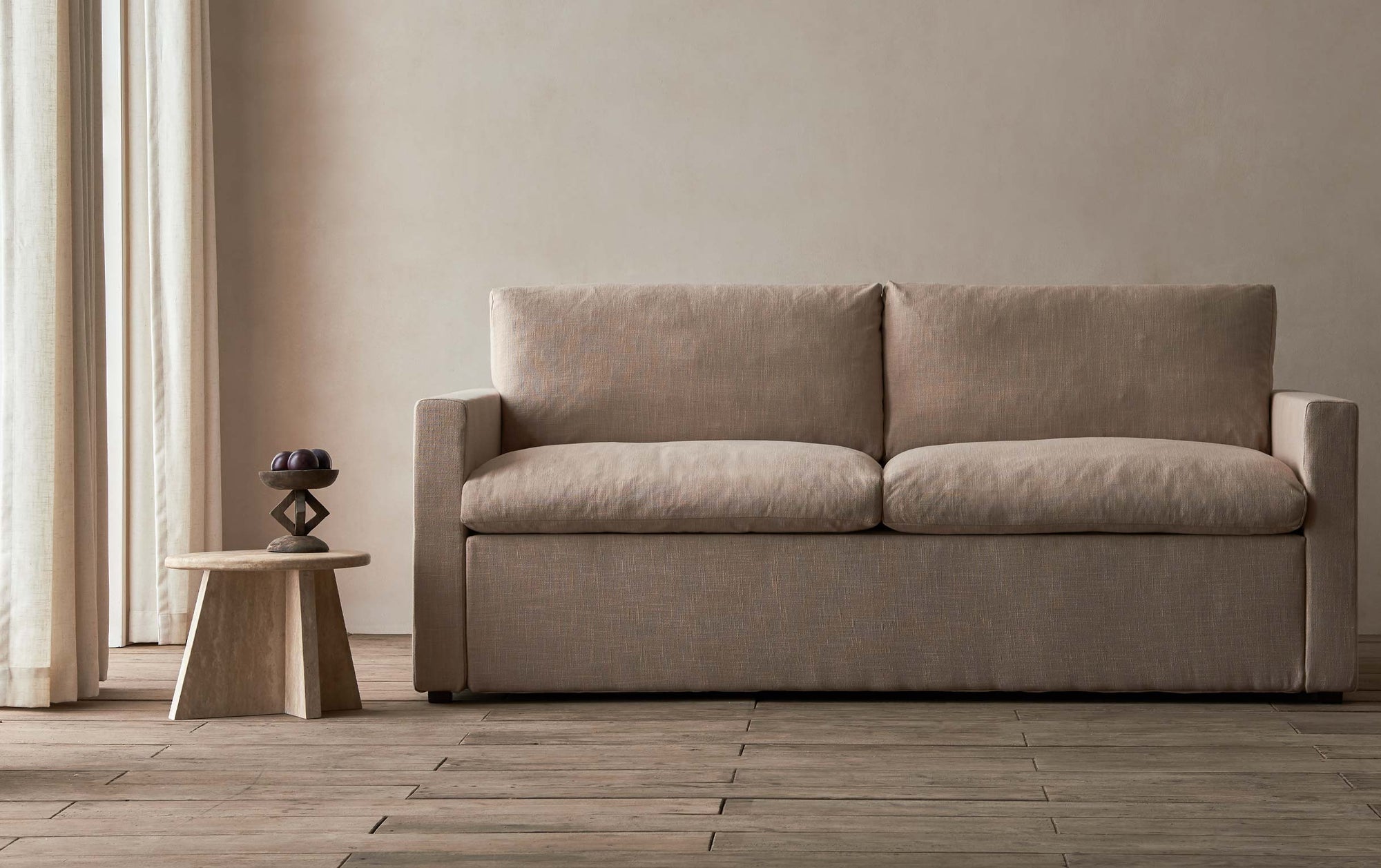 Devyn Sleeper Sofa in Golden Reed, a sandy brown Recycled Poly Linen, in a beige room with a wooden side table.