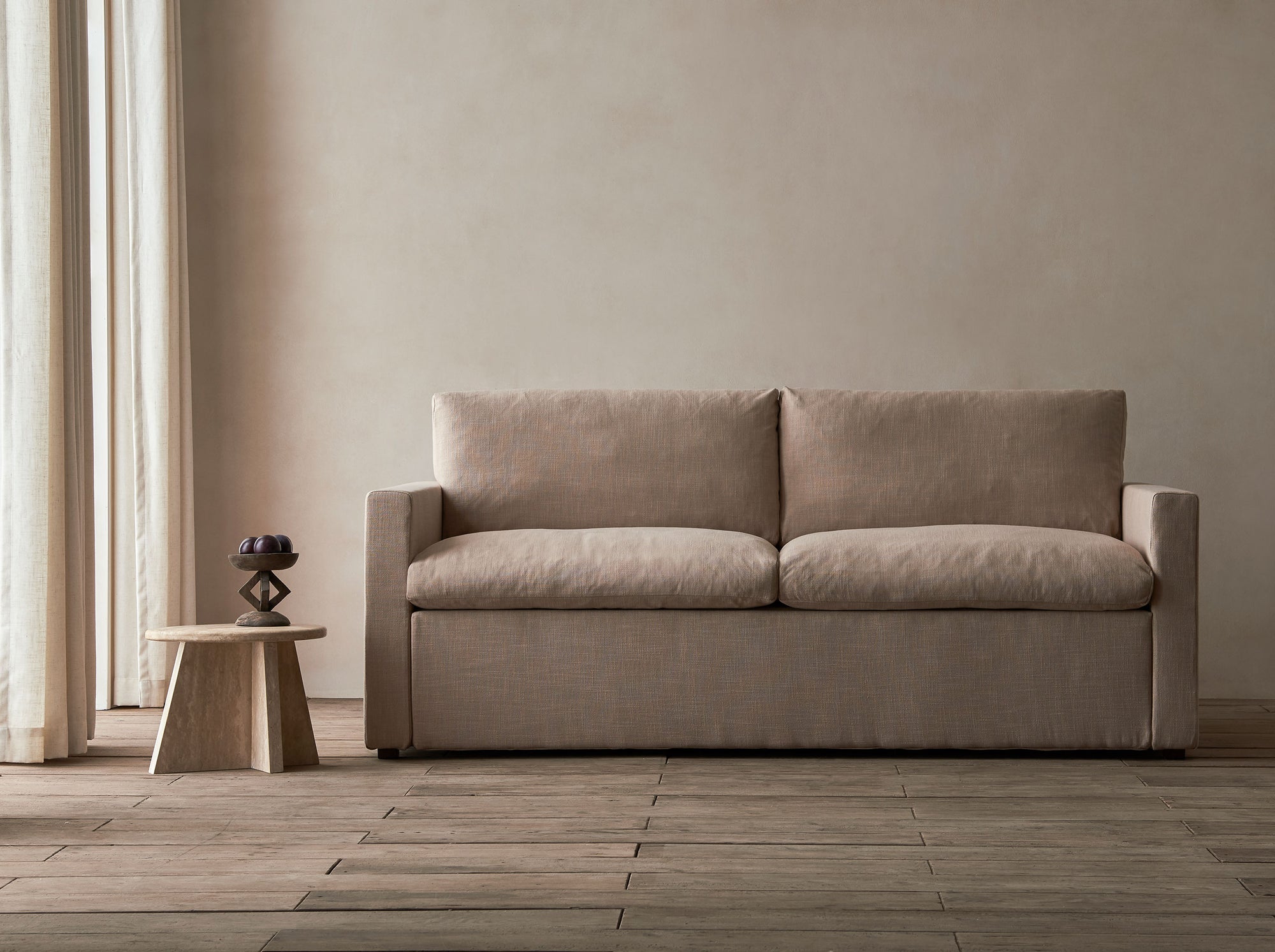 Devyn Sleeper Sofa in Golden Reed, a sandy brown Recycled Poly Linen, in a beige room with a wooden side table.