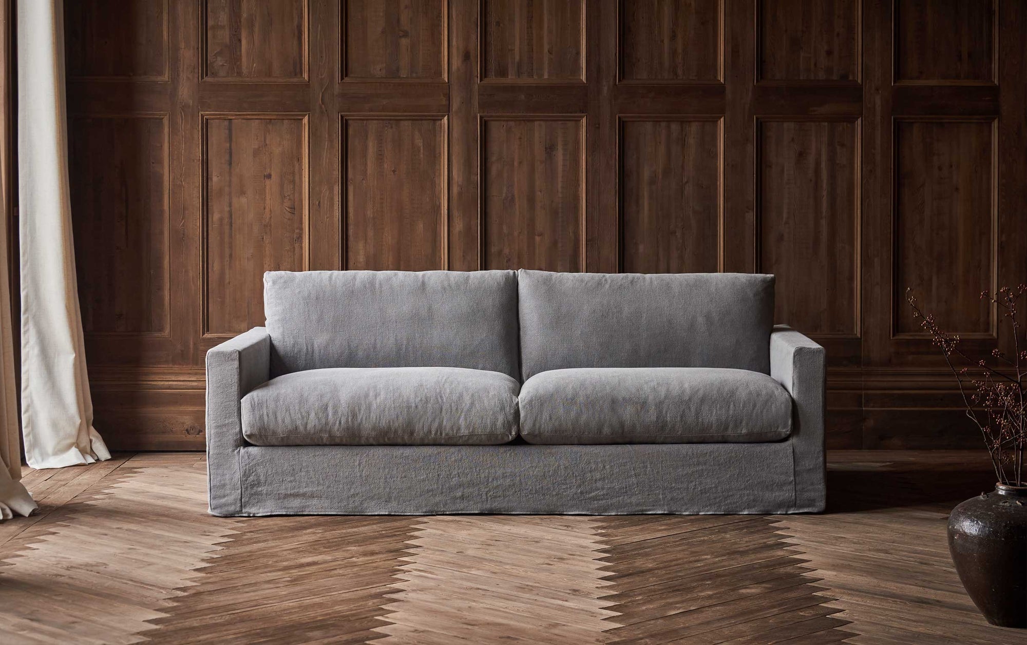 Devyn 84" Sofa in Ink Cap, a medium cool grey Light Weight Linen, placed in a naturally lit, wood-panelled room