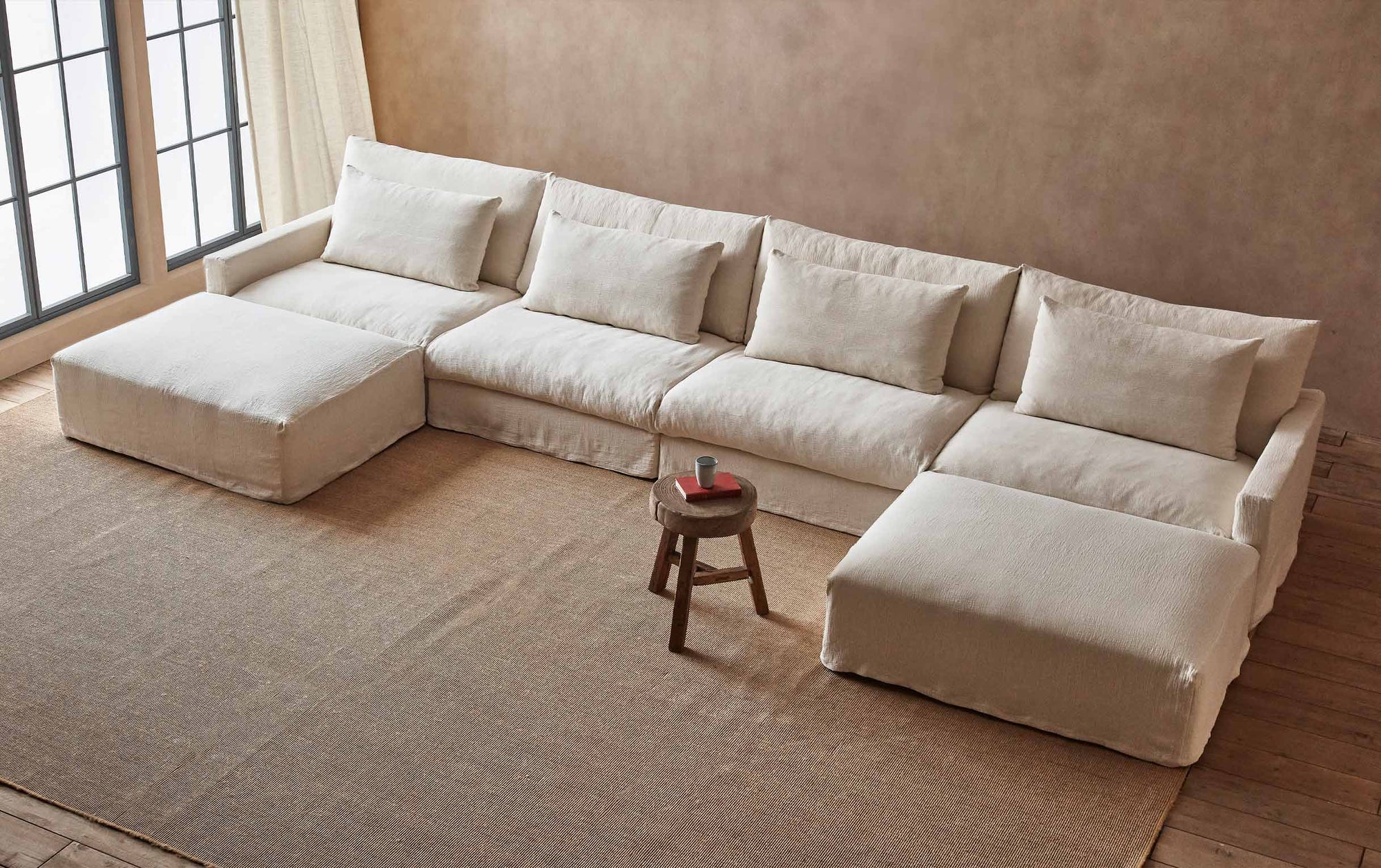 Devyn U-Shape Sectional Sofa in Corn Silk, a light beige Washed Cotton Linen, placed in a sunlit room with a wooden stool