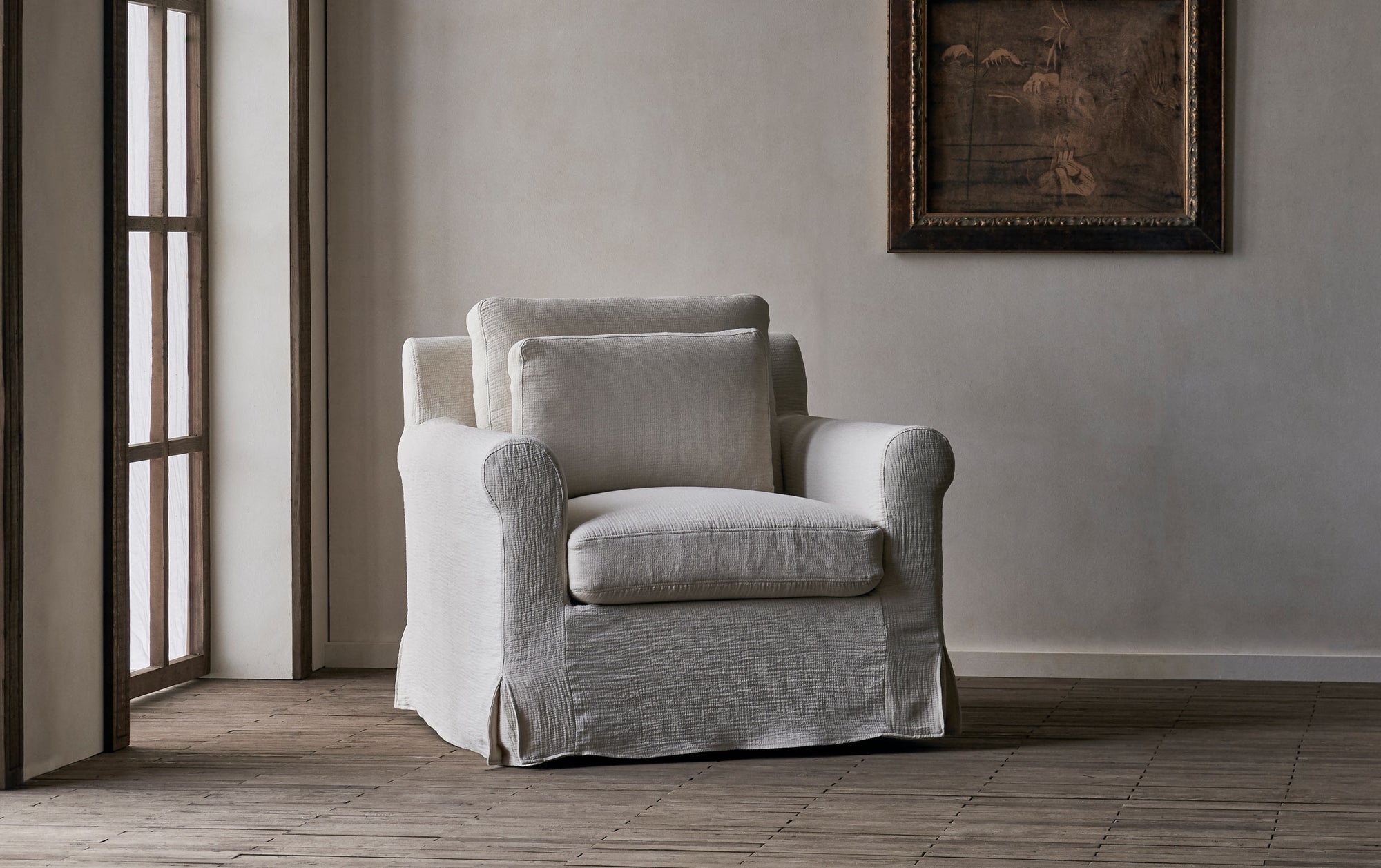 Elias Swivel Chair in Corn Silk, a light beige Washed Cotton Linen, in front of a greige wall with a hanging framed painting