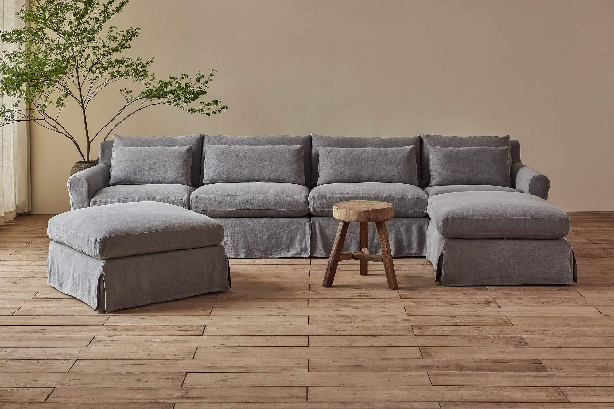 Elias U-Shape Sectional Sofa in Ink Cap, a medium cool grey Light Weight Linen, placed in a room between a potted tree and a stool