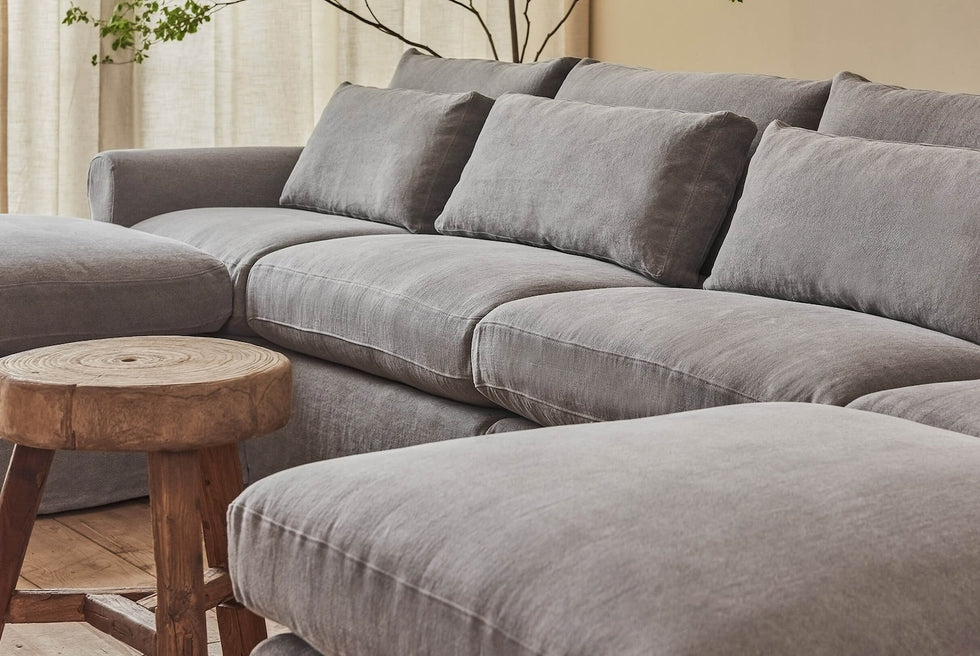 Close up of Elias U-Shape Sectional Sofa in Ink Cap, a medium cool grey Light Weight Linen, placed in a bright room with a small round wooden table