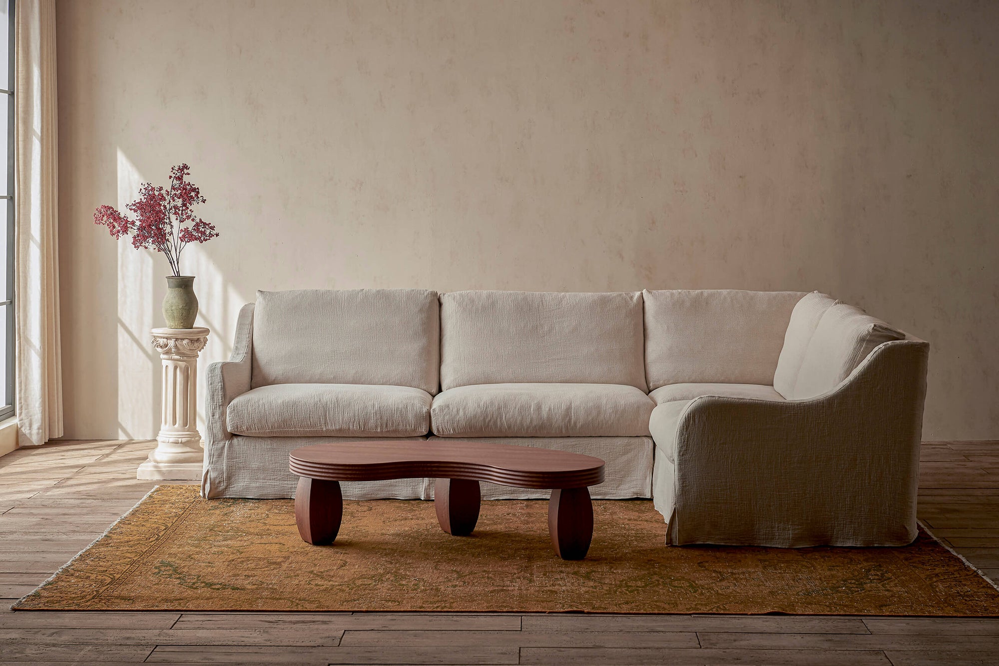 Esmé L-Shape Sectional Sofa in Corn Silk, a light beige Washed Cotton Linen, placed in a sunlit room alongside the PIsces Table