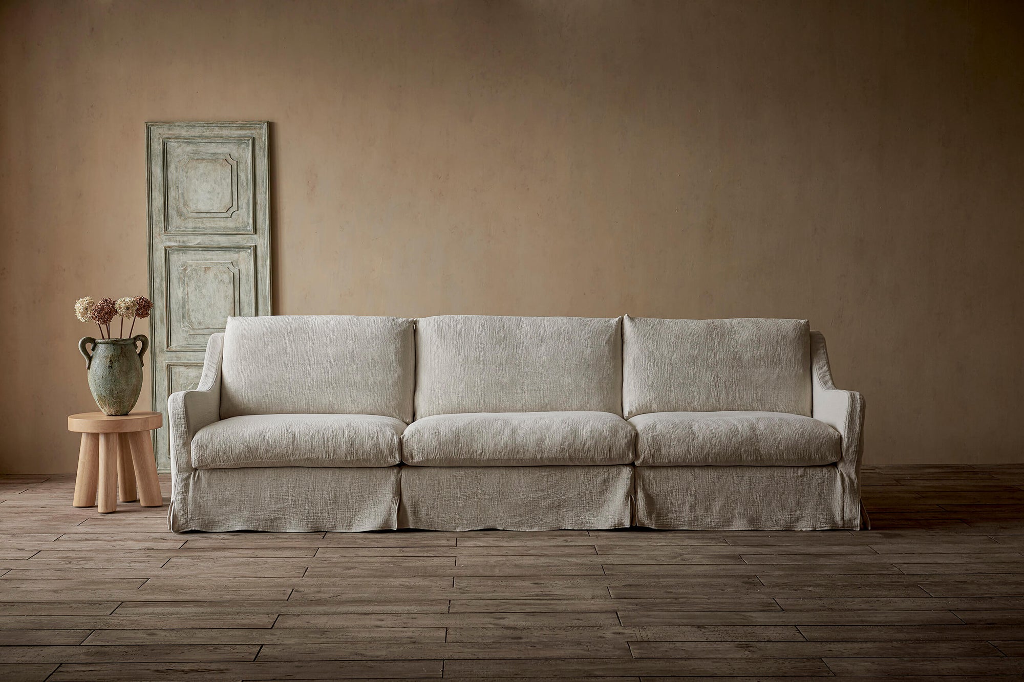 Esmé Sectional Sofa in Corn Silk, a light beige Washed Cotton Linen, placed in a room with a vase of flowers on a stool