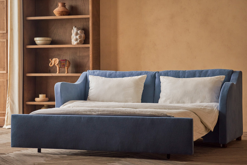 Esmé Sleeper Sofa in Garden Berry, a berry blue Thread-Dyed Cotton Linen, pulled out and made up with white linen bedding