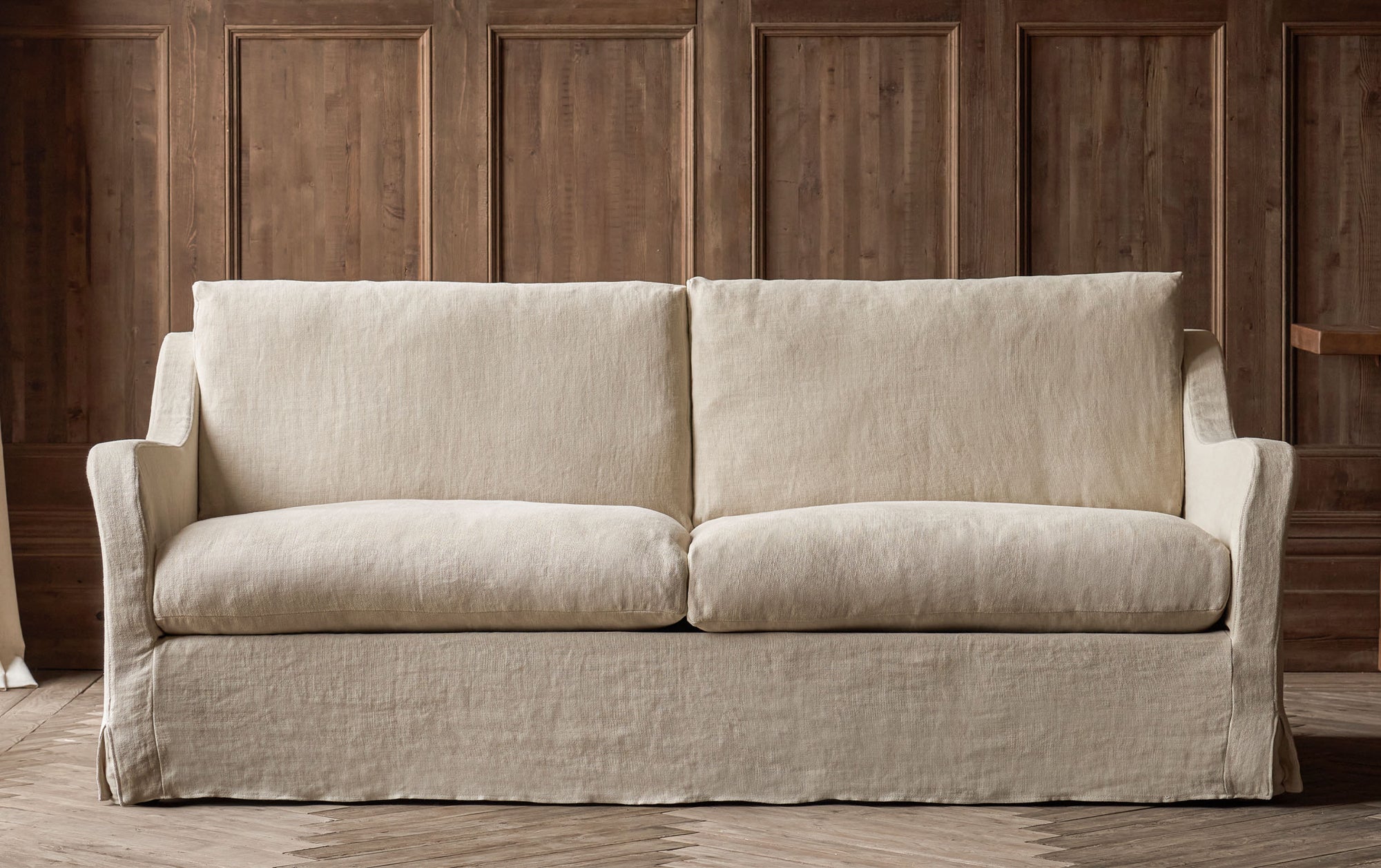 Esmé 96" Sofa in Warm Oatmeal, a light warm beige Medium Weight Linen  placed in front of a wood paneled wall.