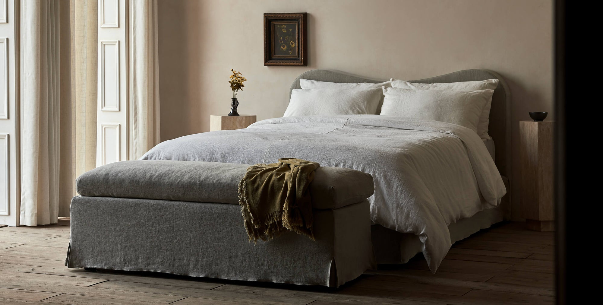 Esmé Storage Bench in Jasmine Rice, a light warm greige Medium Weight Linen, placed in a room at the foot of an Esmé Bed