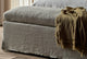 Slide #7 Close up of Esmé Storage Bench in Jasmine Rice, a light warm greige Medium Weight Linen, holding a green throw blanket and placed in a room at the foot of an Esmé Bed