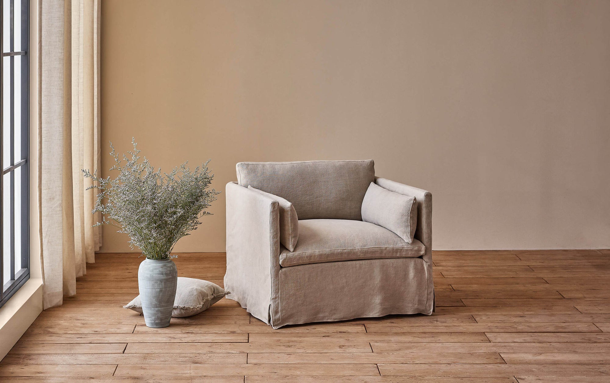 Gabriel Chair in Jasmine Rice, a light warm greige Medium Weight Linen, placed in a sunlit room next to flowers in a vase