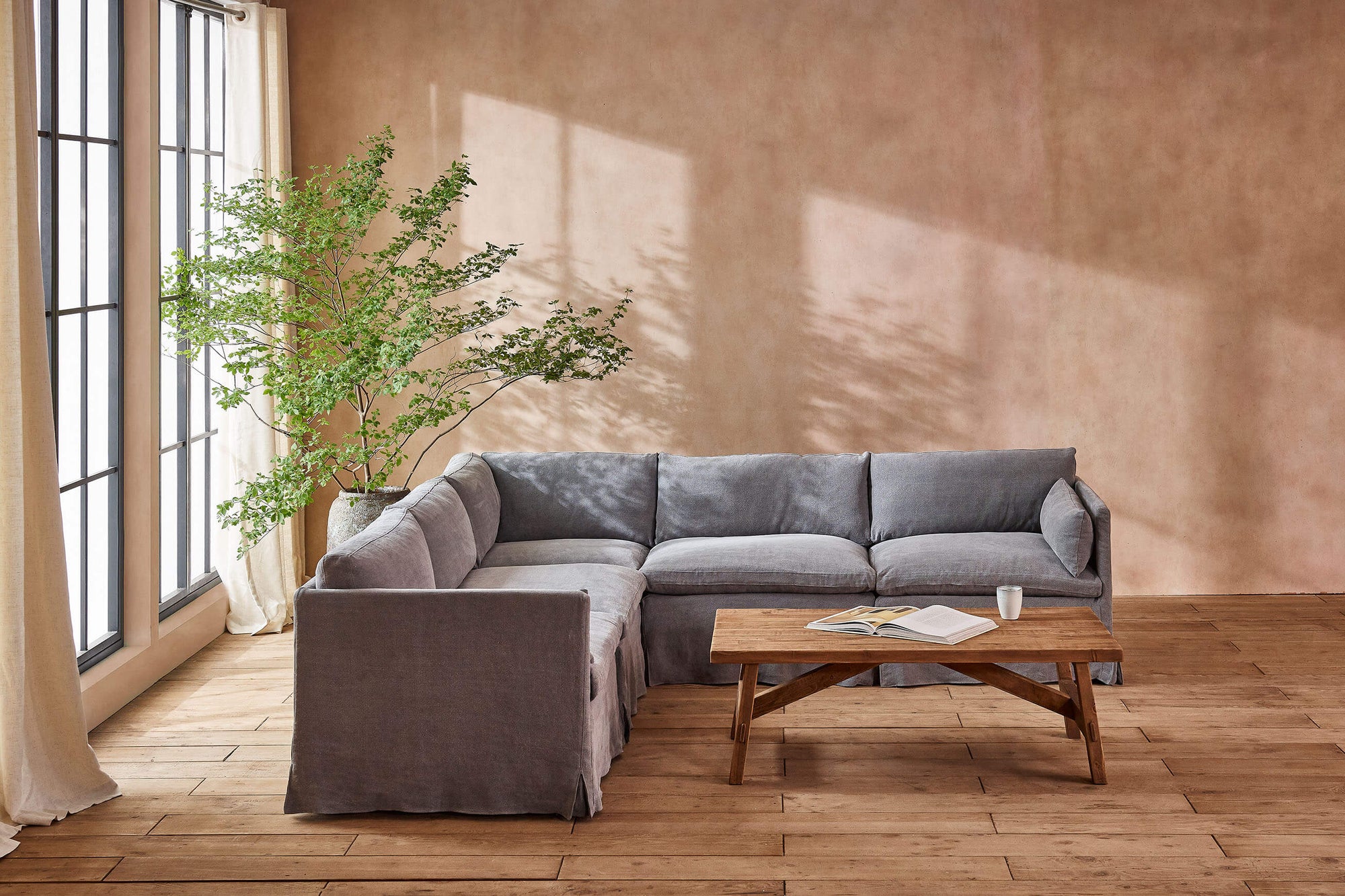 Gabriel Corner Sectional Sofa in Ink Cap, a medium cool grey Light Weight Linen, placed in a sunlit room around a coffee table