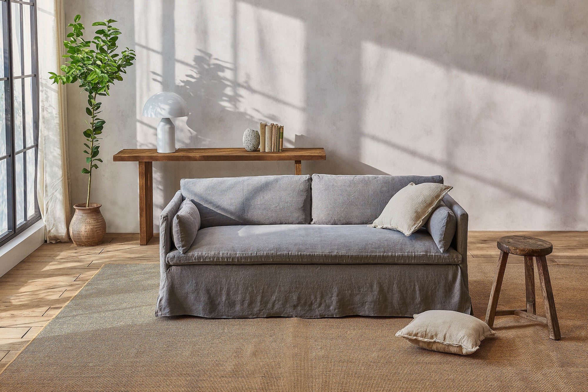 Gabriel 72" Sofa in Ink Cap, a medium cool grey Light Weight Linen, with a light taupe throw pillow, in front of a wooden console table and large potted plant