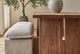 Slide #7 Close up of Kai Dining Table in 100% Reclaimed Austrian Heritage Oak, a medium, bosc pear shade with earthy undertones, placed in a sunlit room with a Neva Dining Bench and a potted tree