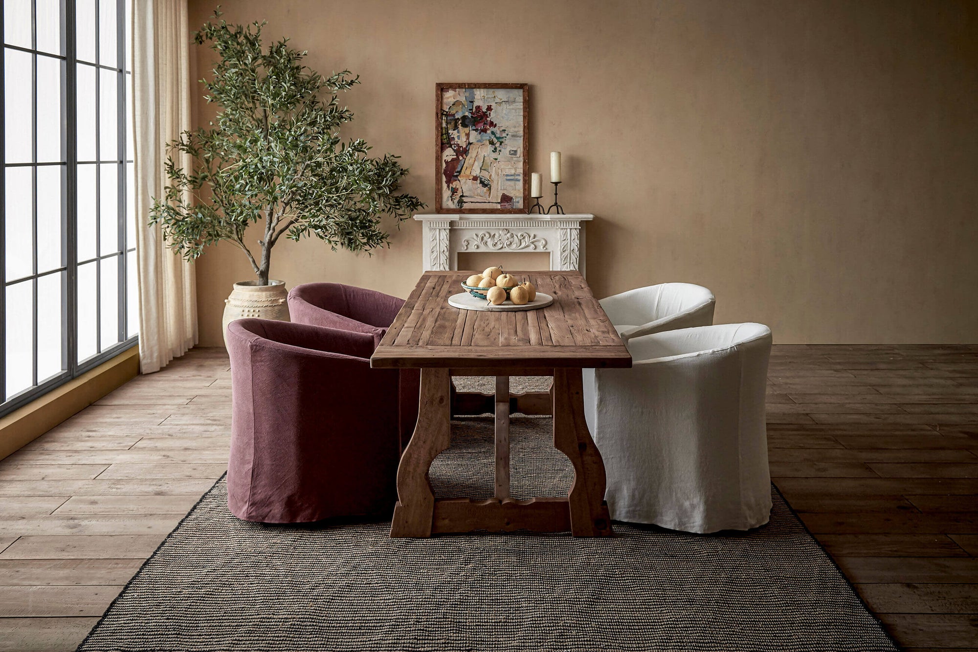 Four Ziki Dining Chairs placed around the Leona Dining Table in Heritage Pine in a sunlit room decorated with a potted tree and a painting on a mantle