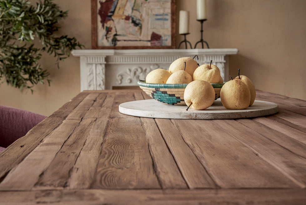 Close up of Leona Dining Table in 100% Reclaimed Chinese Heritage Pine, a medium, bosc pear shade with earthy undertones, placed in a decorated room with a bowl of pears on it.