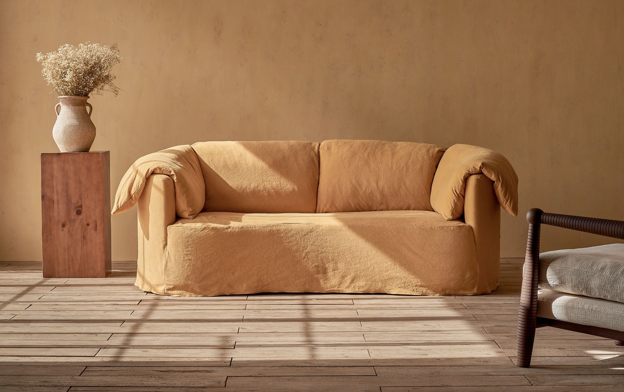 Loula Sofa in Honey Bee, a saffron yellow Thread-Dyed Cotton Linen, placed in a sunlit room beside a vase and pillar