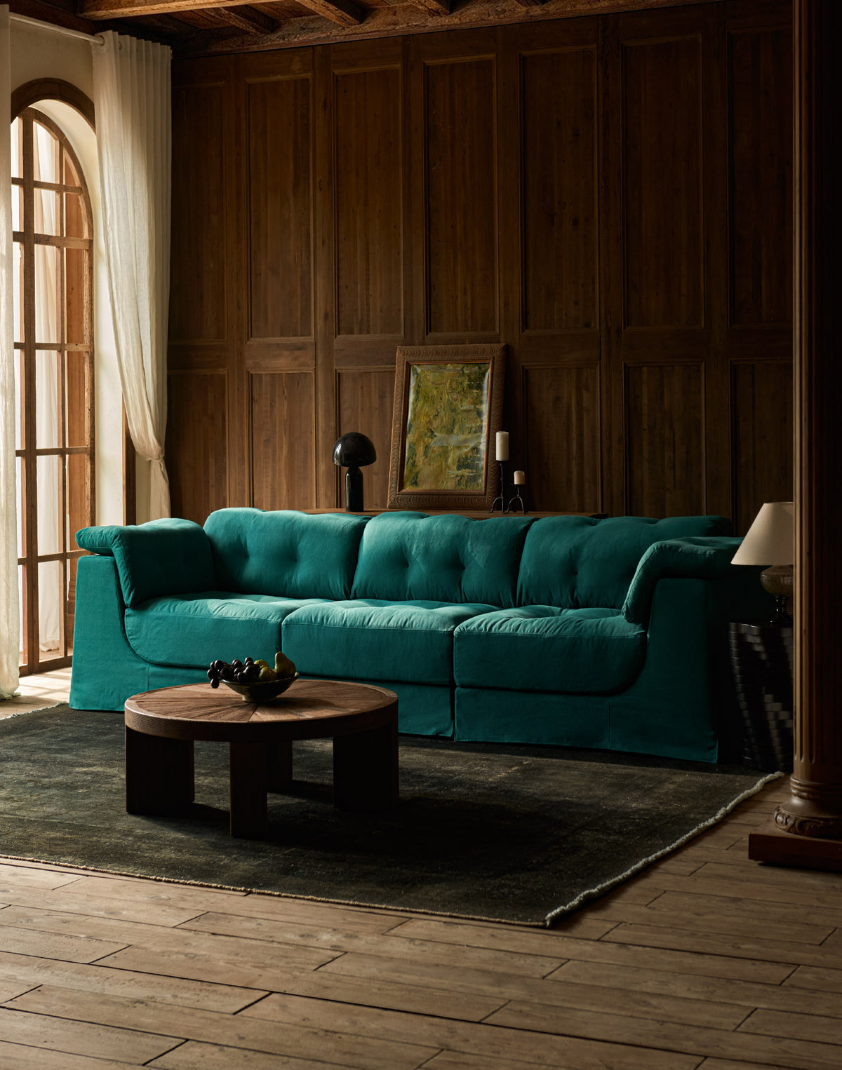 A Sixpenny Mo sectional sofa, in thread-dyed cotton linen, in ivy league, dark wood-paneled living room with a wooden coffee table and a dark rug.