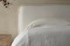 Slide #6 Close up of Neva Queen Bed in Water Lily, a white Light Weight Linen with warm undertones, made in white linen bedsheets and placed next to a stone side table
