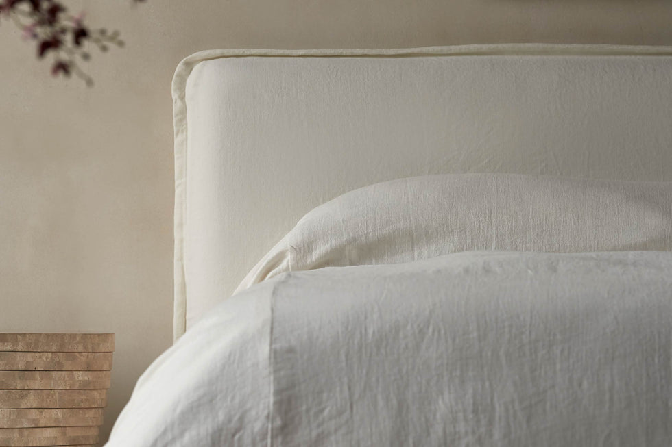 Close up of Neva Queen Bed in Water Lily, a white Light Weight Linen with warm undertones, made in white linen bedsheets and placed next to a stone side table
