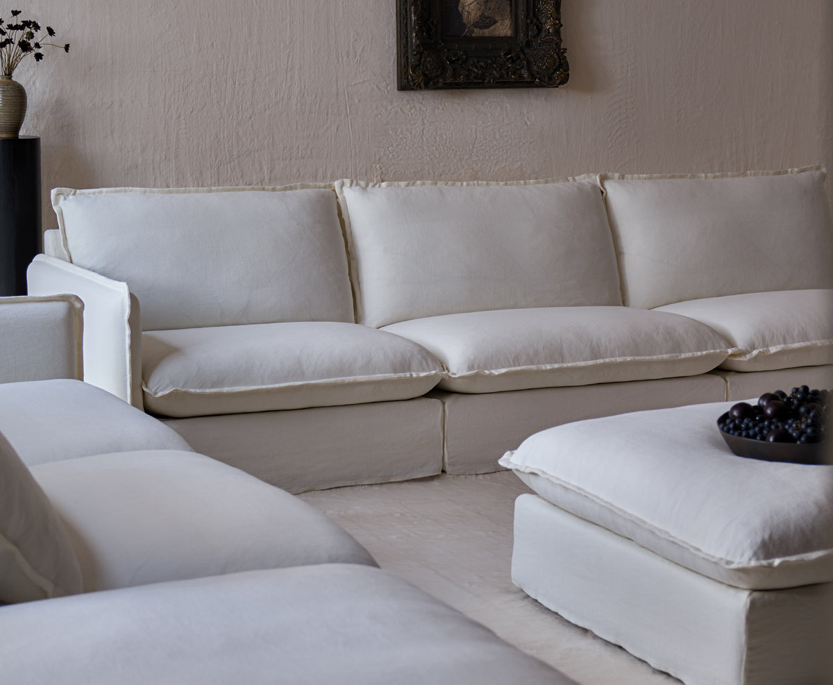A Sixpenny Neva chaise sectional sofa in water lily with a matching ottoman in a minimalist, modern living room with textured beige walls.