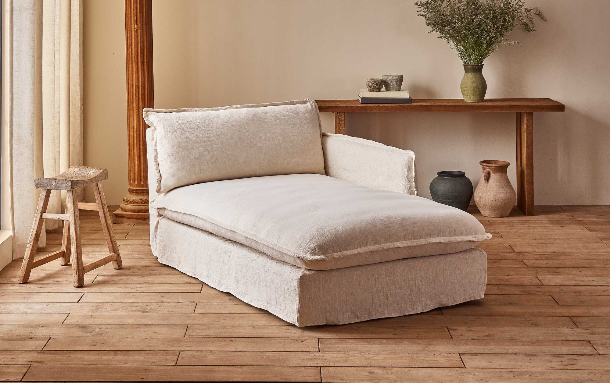 Neva Daybed in Corn Silk, a light beige Washed Cotton Linen, placed in a sunlit room with a decorated Kai Console Table and a wooden stool.