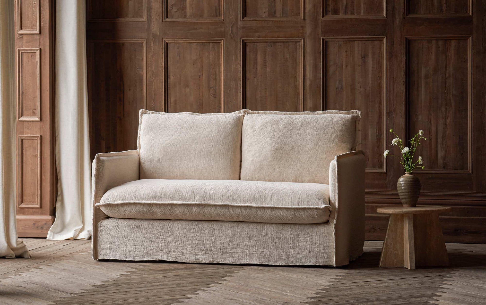 Neva 62" Loveseat in Corn Silk, a light beige Washed Cotton Linen placed beside a side table with a potted plant