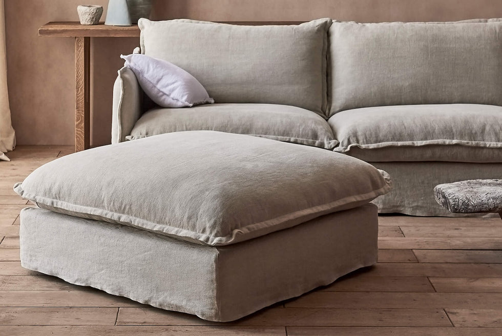 Close up of Neva Sectional Ottoman in Jasmine Rice, a light warm greige Medium Weight Linen, placed in a bright room in front of a Neva Sectional, in front of a decorated console table