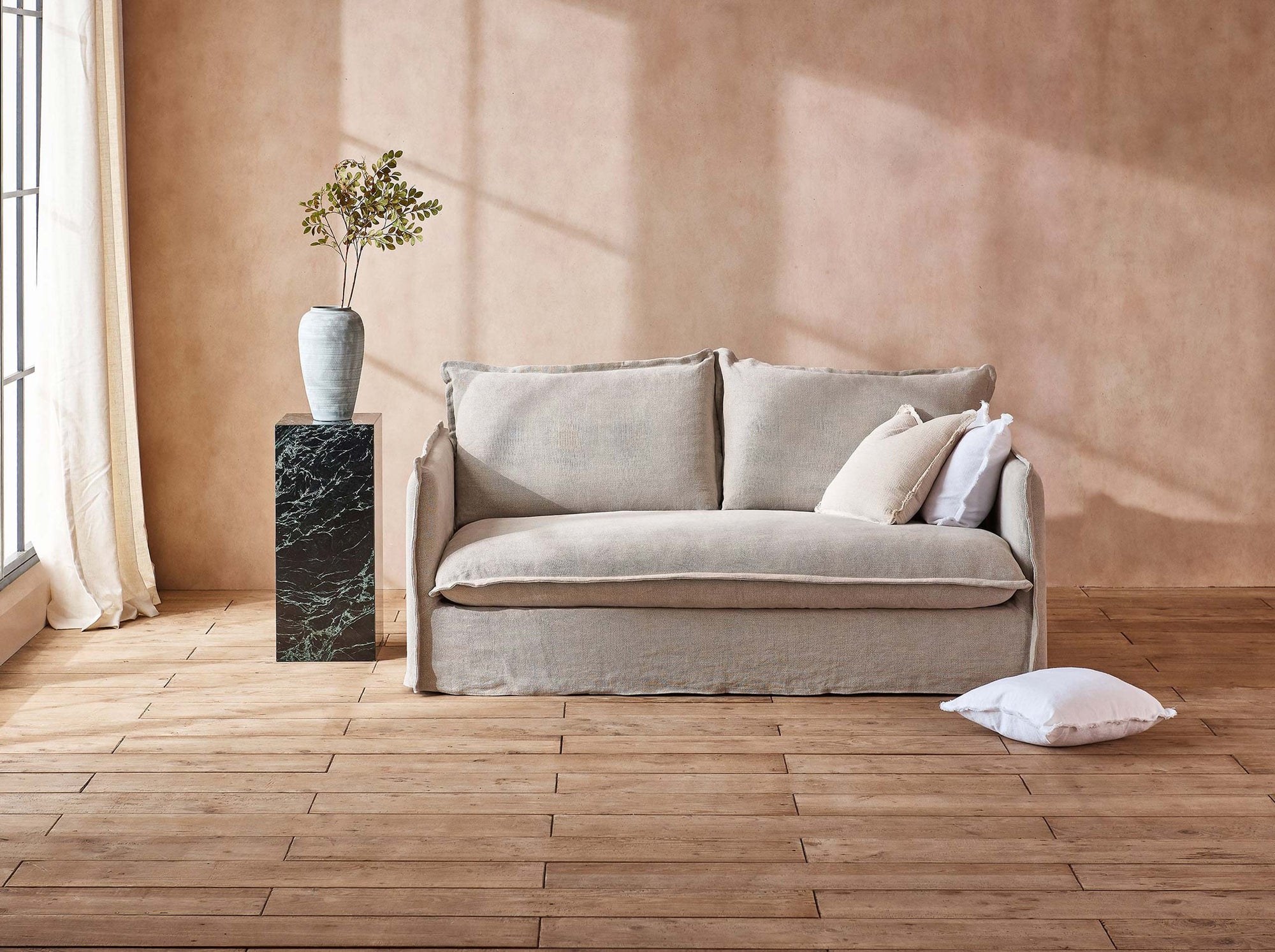 Neva 72" Sofa in Jasmine Rice, a light warm greige Medium Weight Linen, placed in a sunlit room next to plants in a vase on a side table