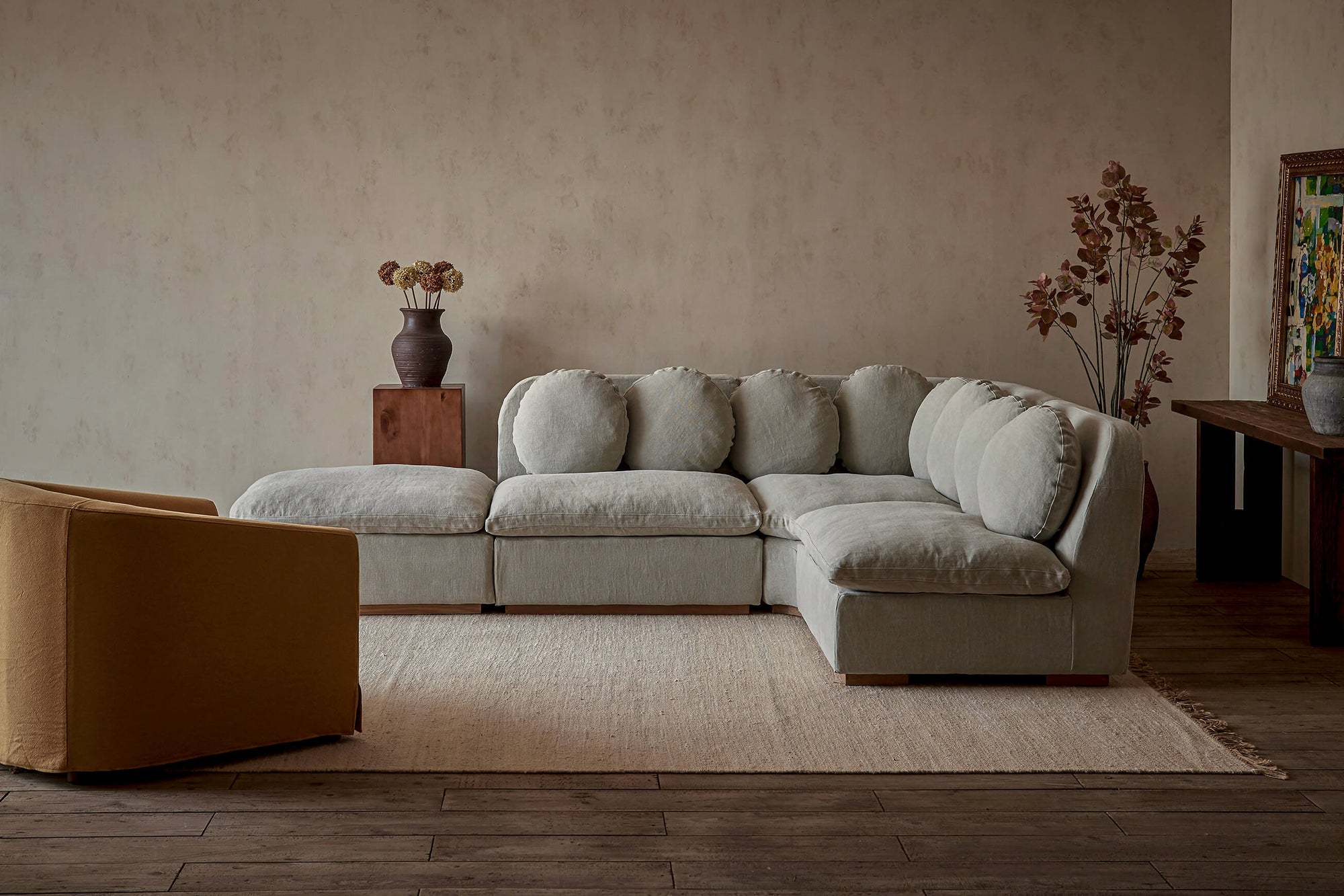 Olea L-Shape Sectional Sofa in Jasmine Rice, a light warm greige Medium Weight Linen, placed in a room decorated with vases, flowers, and a chair.