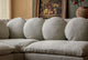 Slide #6 Close up of Olea Short Corner Sectional in Jasmine Rice, a light warm greige Medium Weight Linen, placed in front of a console table with a framed piece of art and a vase of flowers