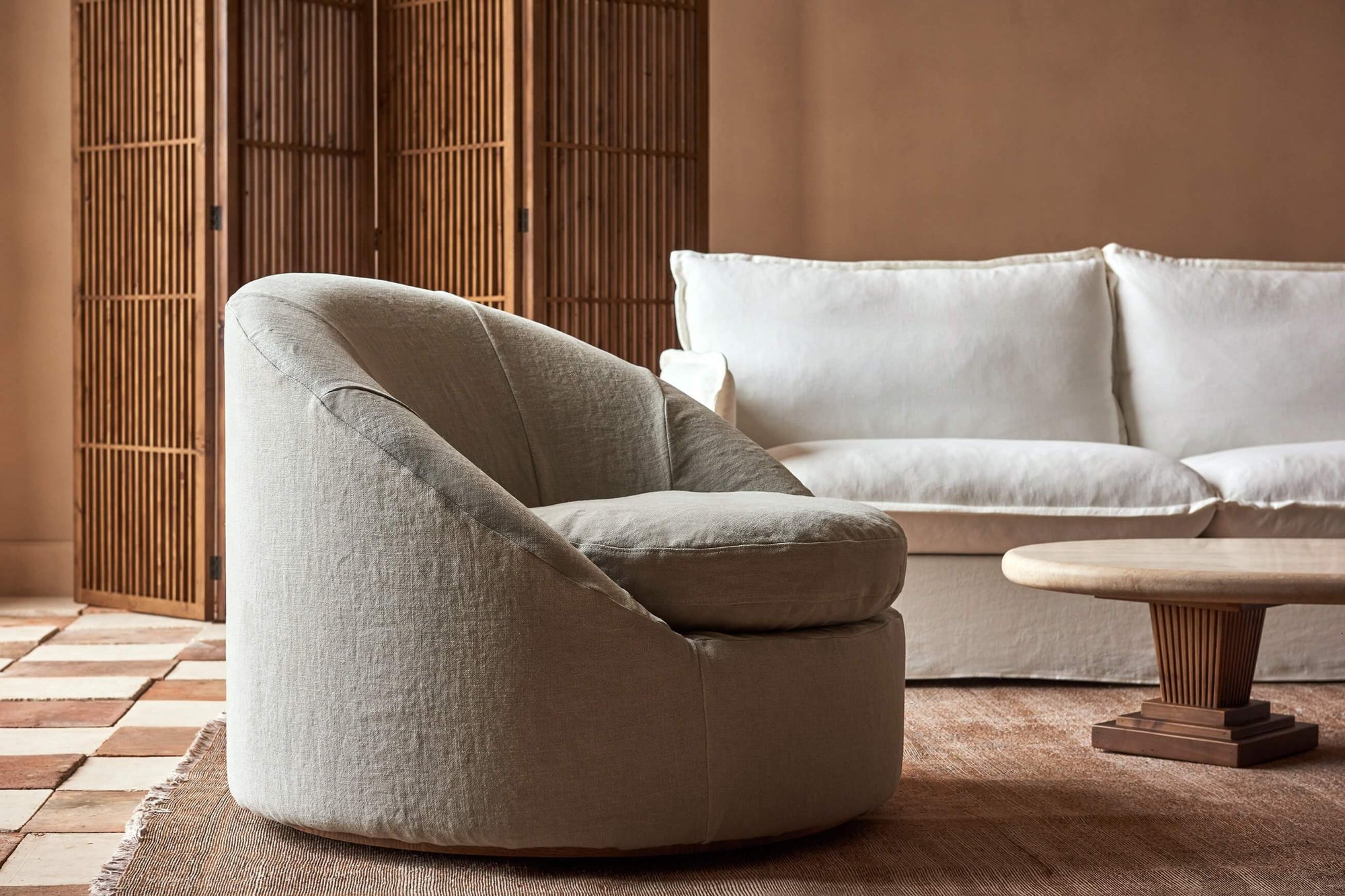 Olea Swivel Chair in Jasmine Rice, a light warm greige Medium Weight Linen placed in a sunlit room in front of a Neva Sofa and Cordelia Coffee Table