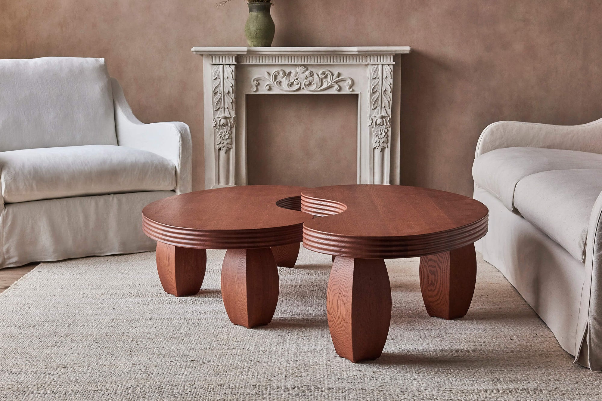 A Short and Tall Pisces Coffee Table in Spiced Oak placed next to each other in front of a white mantle, surrounded by an Esmé Chair and Sofa.