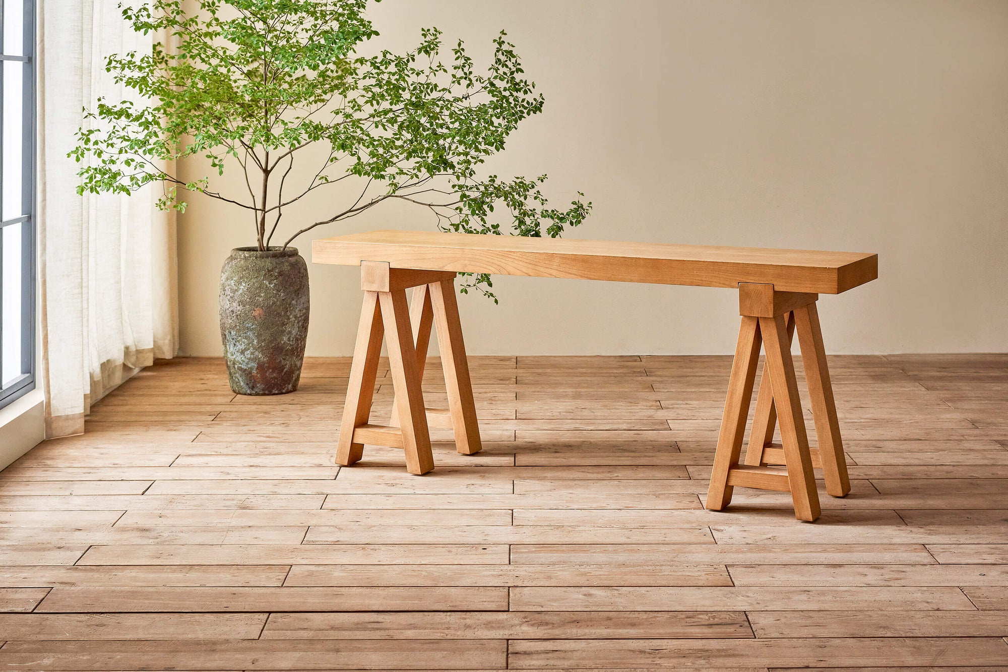 Rylance Console Table in Tinted Oak, a golden, wheat-colored 100% American red oak, placed in a bright room next to a potted tree