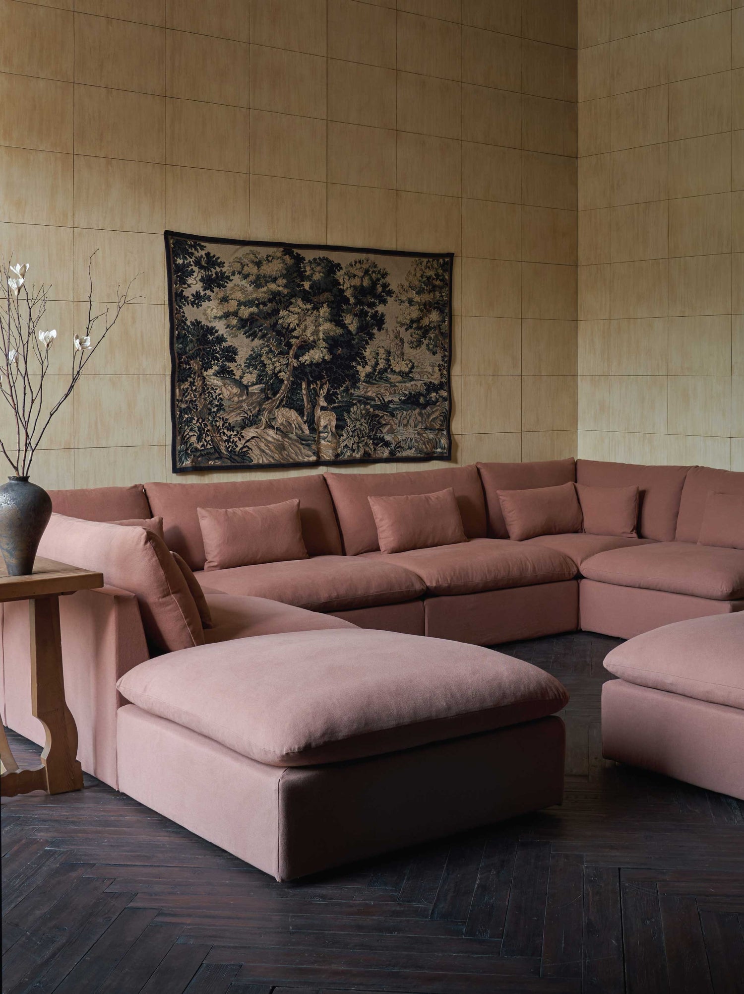Sixpenny Aria Grande U-Shape Sectional in a room with a wall tapestry and wooden side table.