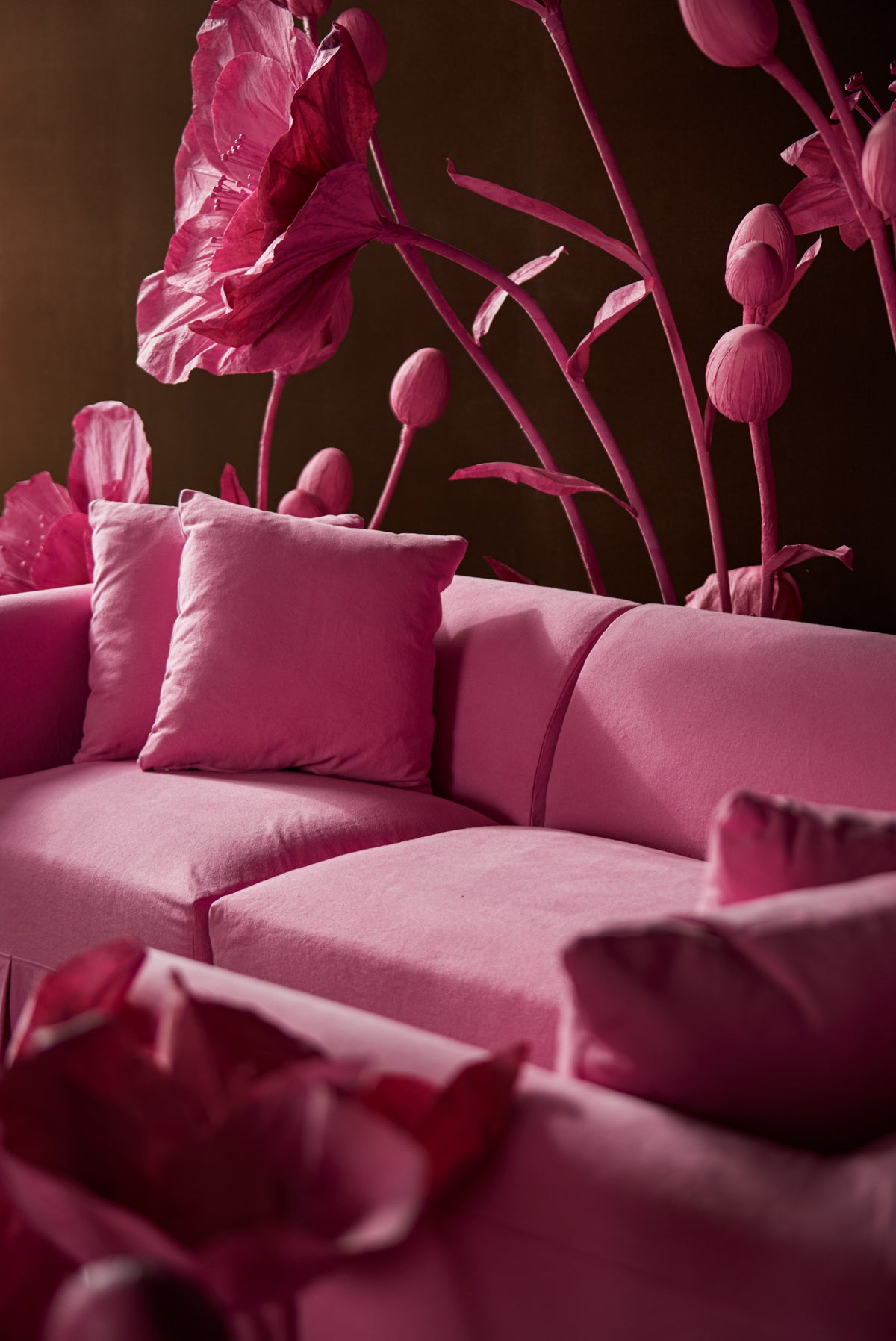 A pink Dalia Sectional in pink lady with matching throw pillows in a dimly lit room, set against a dark wall decorated with oversized pink floral wall art.