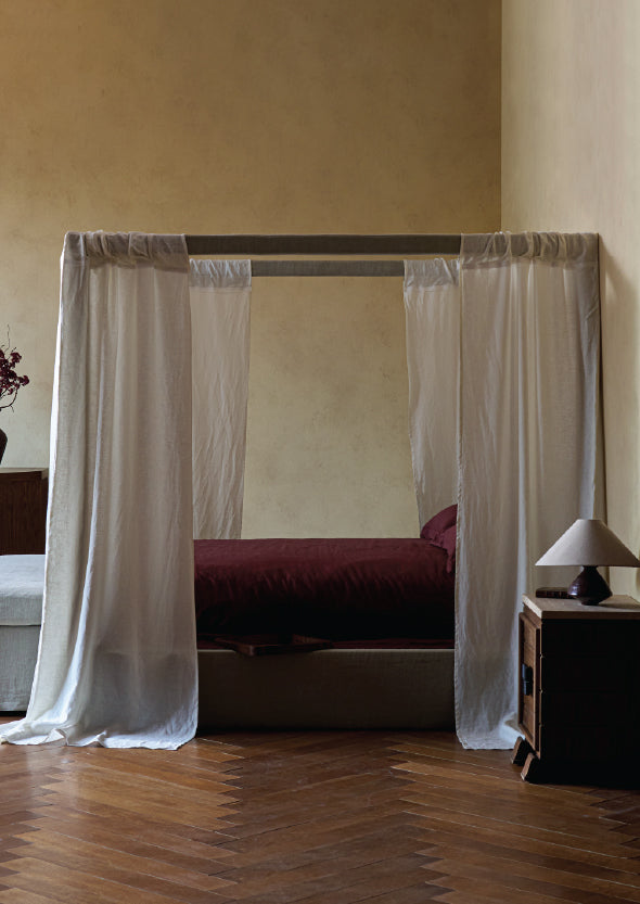 Bedroom with sixpenny Florette bed with white curtains, wooden floor, and neutral walls.